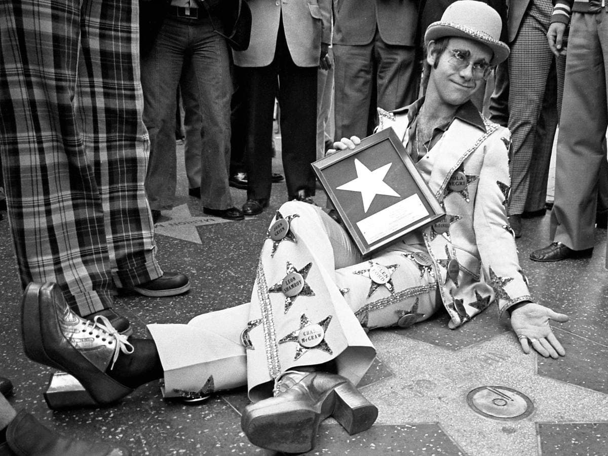 Elton John sitting on the pavement beside his Walk of Fame star in 1975