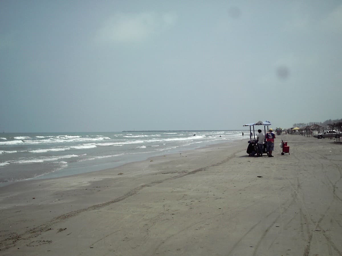A wide grey beach and surf under an overcast sky