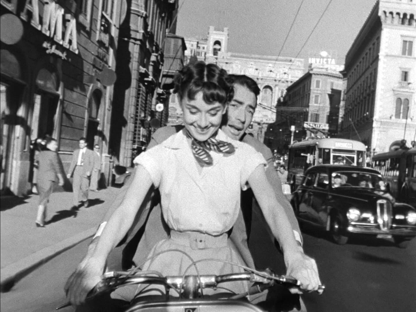 Audrey Hepburn riding a scooter with Gregory Peck behind her