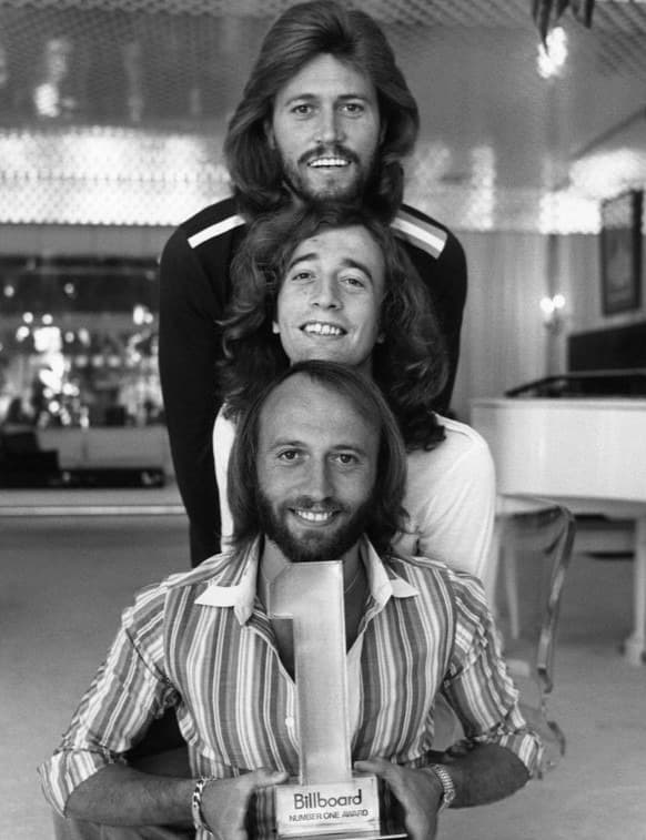 Three smiling bearded brothers stacked one above another, the front one holding a number-one award