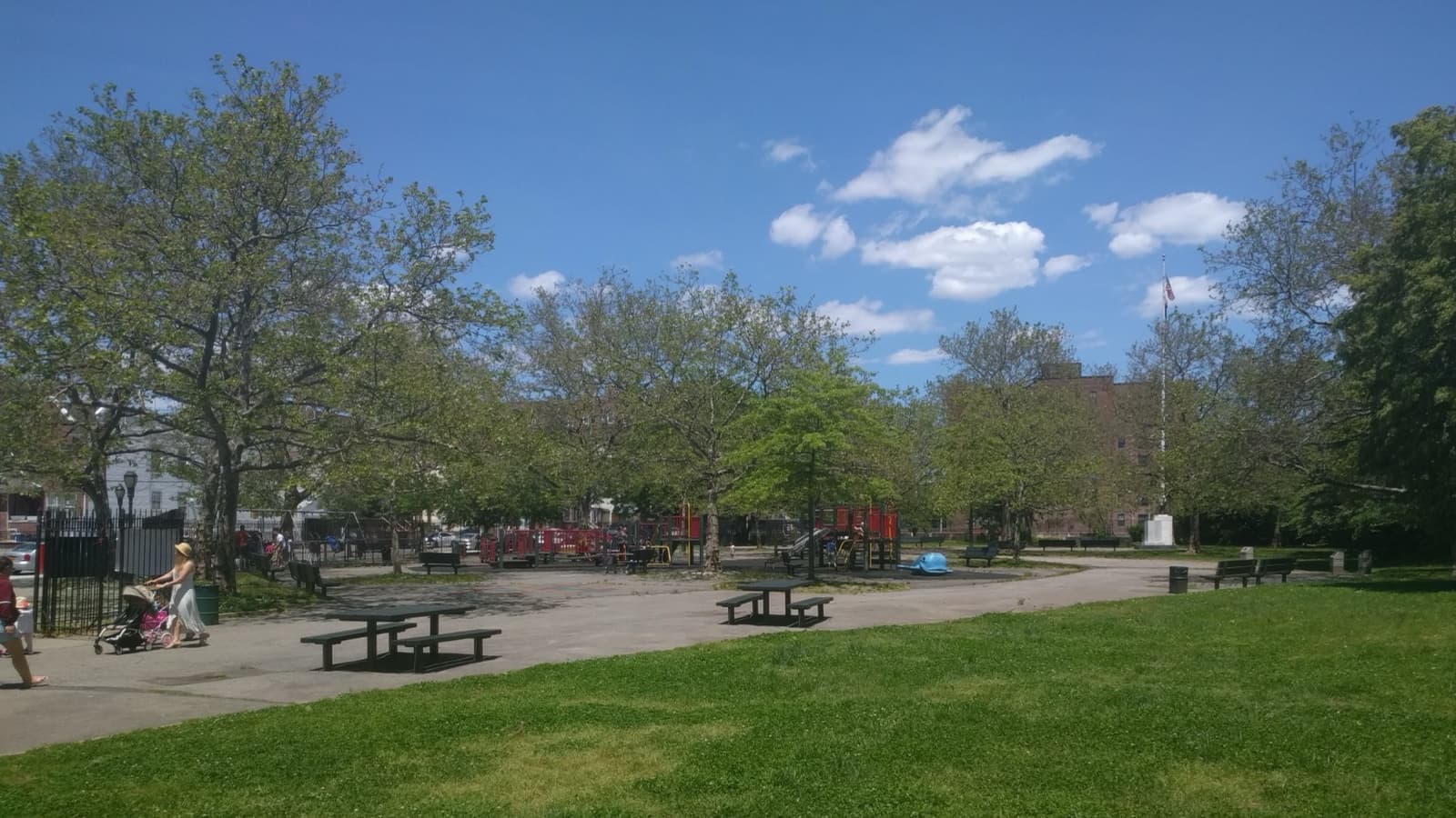 A grassy park with trees, picnic tables and a paved path under a blue sky
