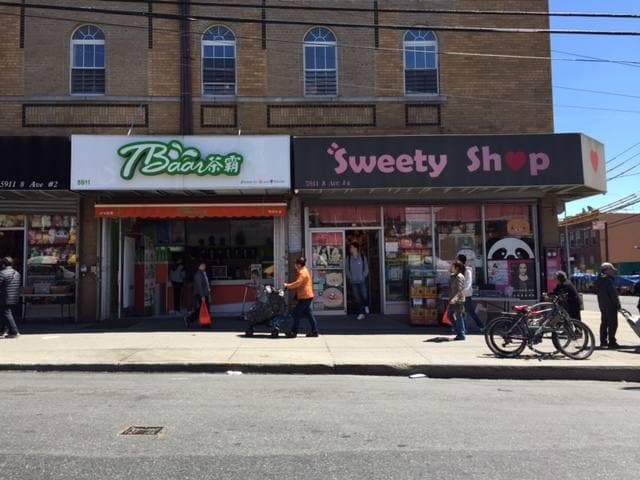 A Brooklyn avenue corner with shopfronts, signs and parked cars
