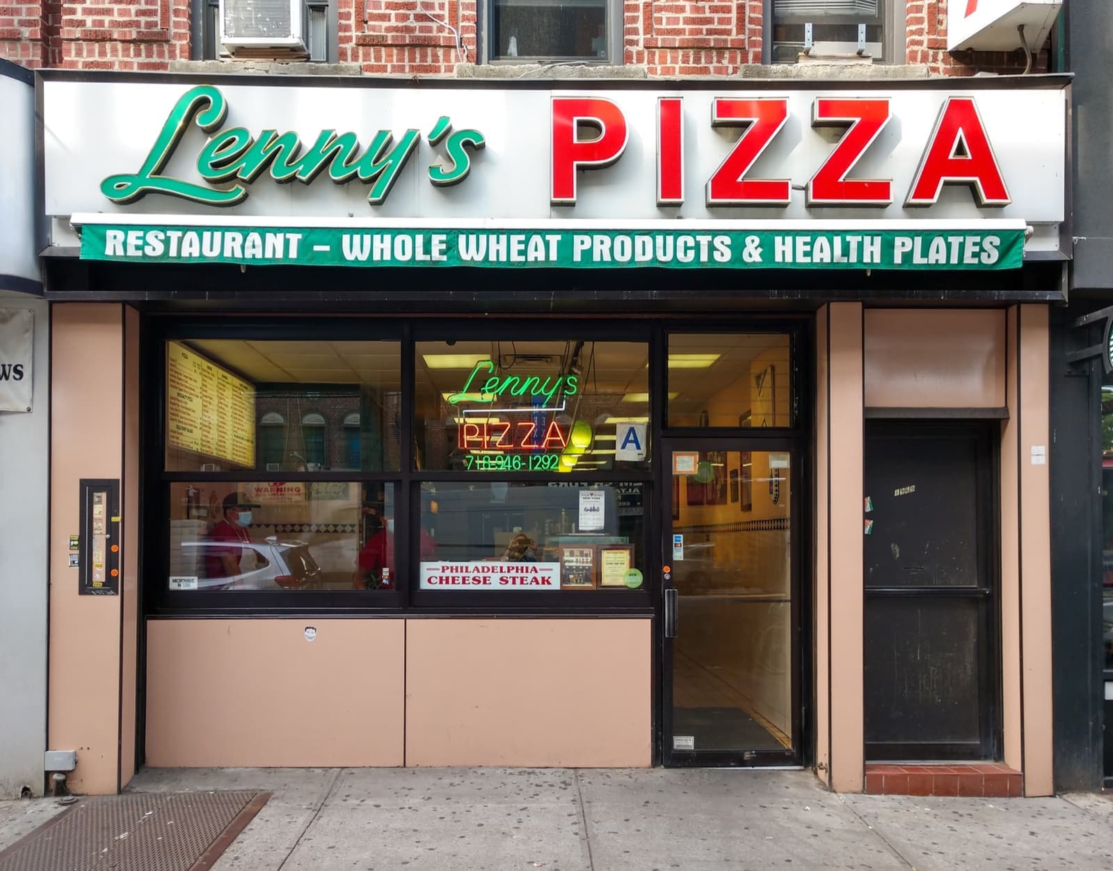 A small pizzeria shopfront with a green and red sign reading Lenny’s Pizza and a neon sign in the window