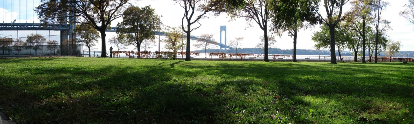 A wide lawn with trees along the water, the long bridge across the horizon
