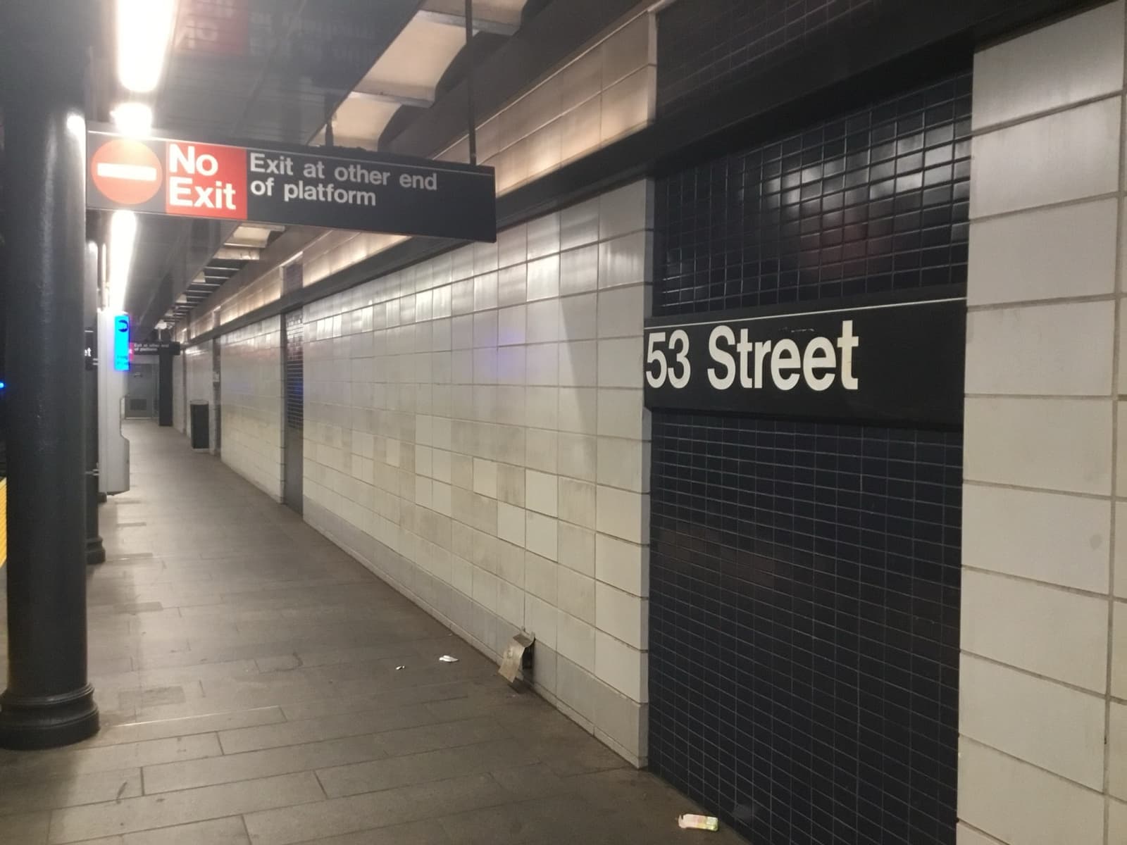 A clean subway platform with white and navy tiles and a sign reading 53 Street