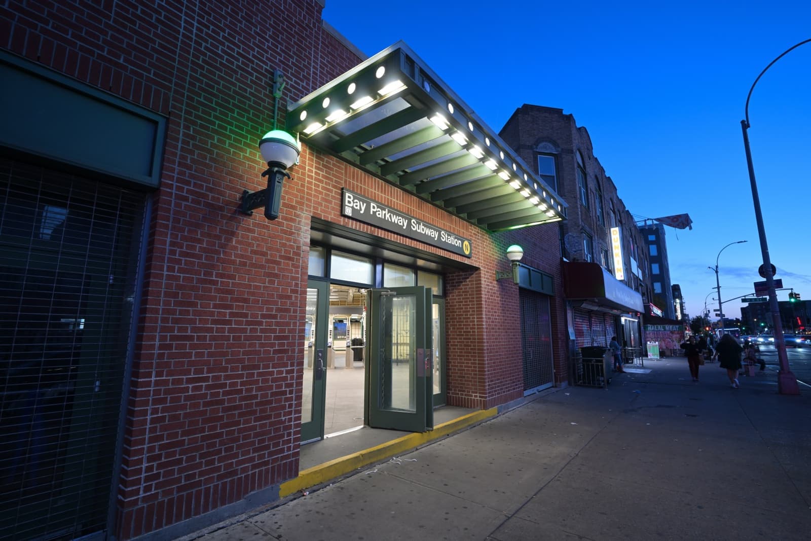 A brick subway station house with a lit green canopy under a deep blue evening sky