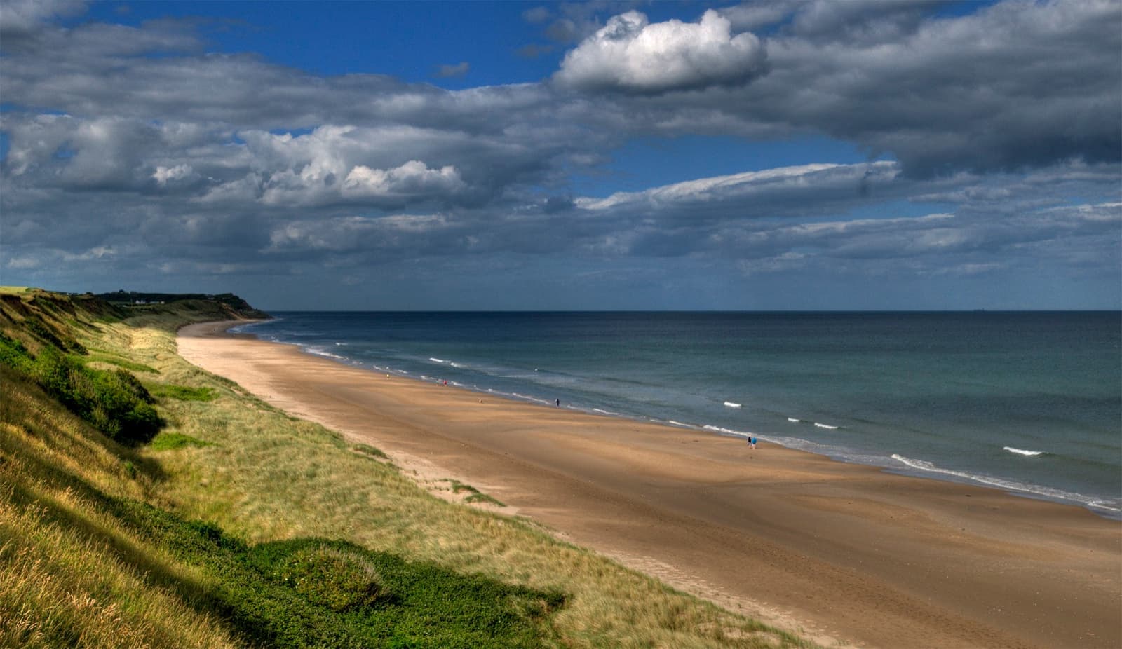 A long empty sand beach below grassy dunes under a big sky