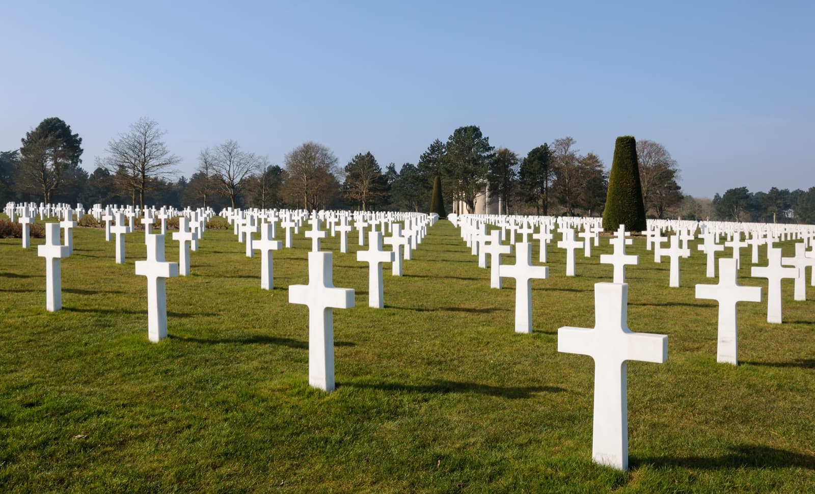 Rows of white marble crosses on a green lawn under a blue sky