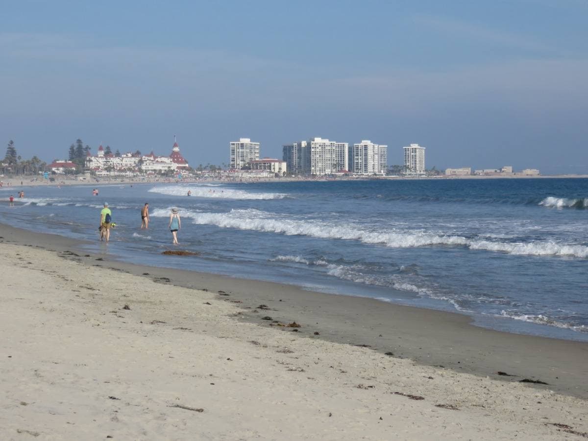 A wide sandy beach with low surf and the red-roofed Hotel del Coronado in the distance