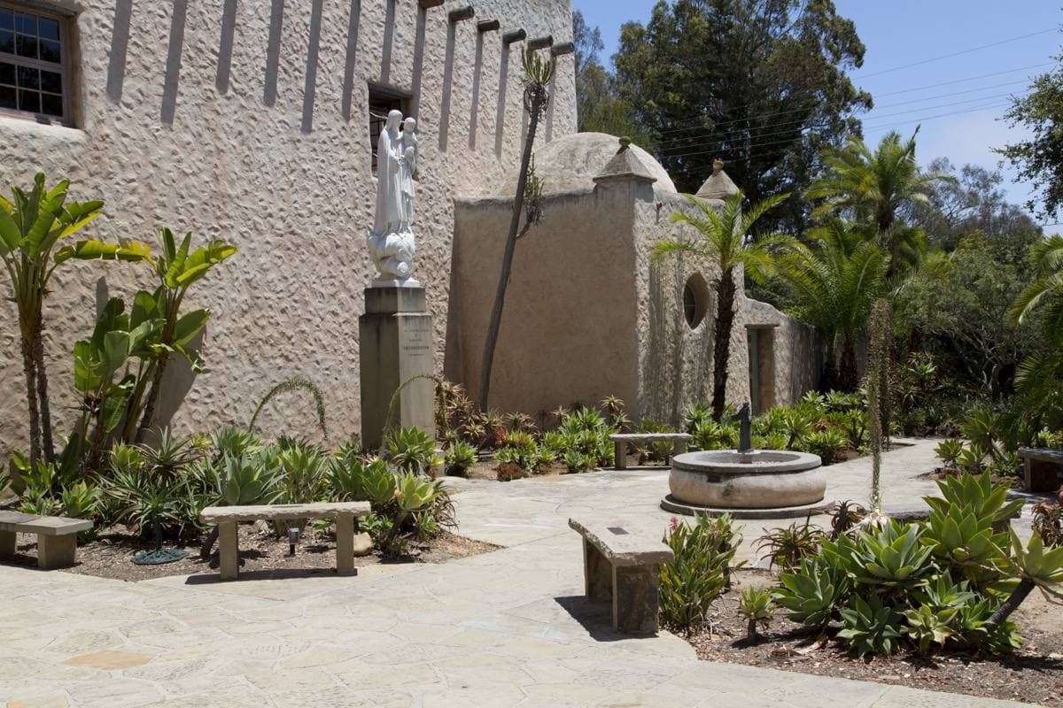 The stone courtyard of a Spanish-style church in Montecito, with a statue, a fountain and succulents