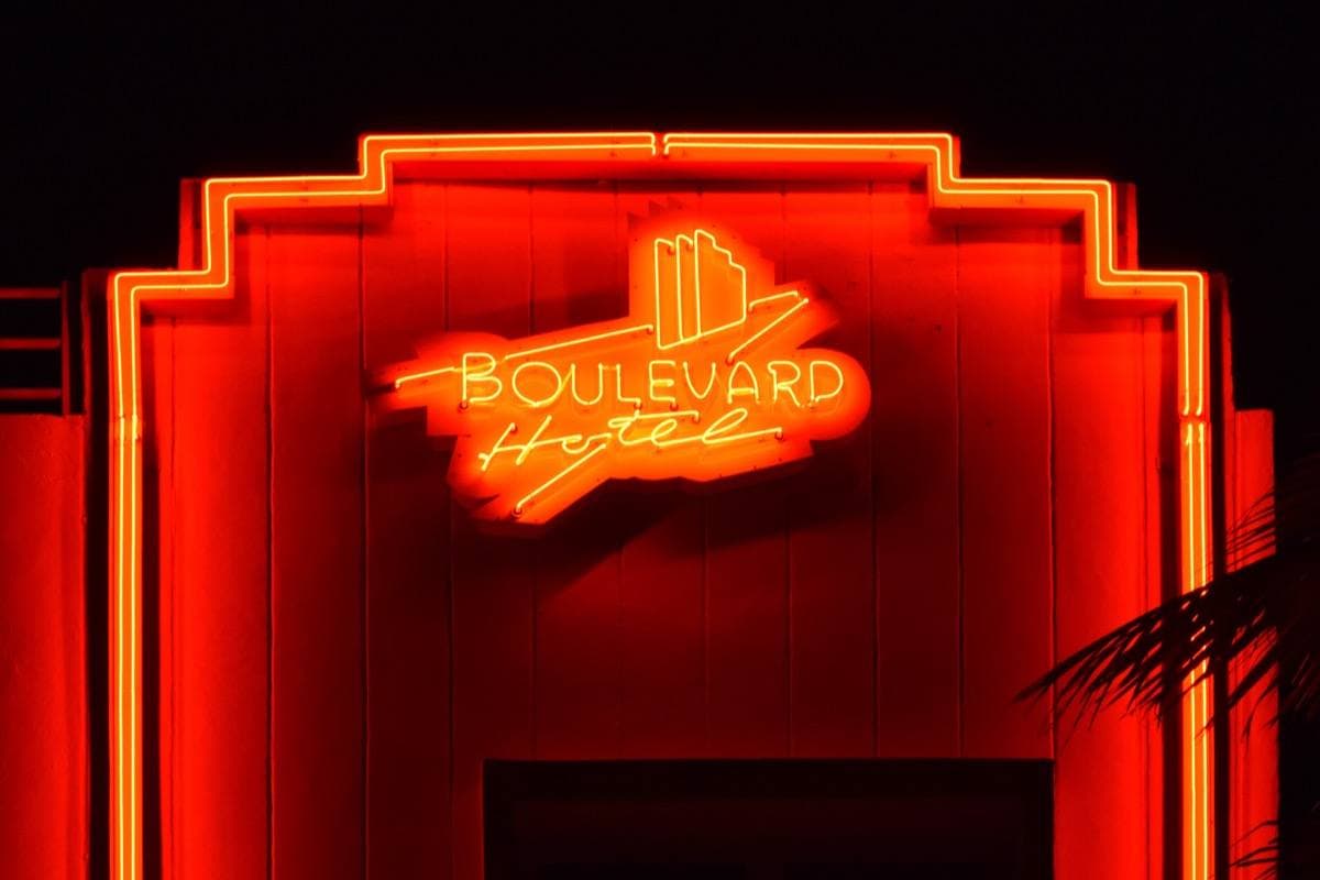 Red neon tubes framing a stepped doorway, with the hotel name in orange script