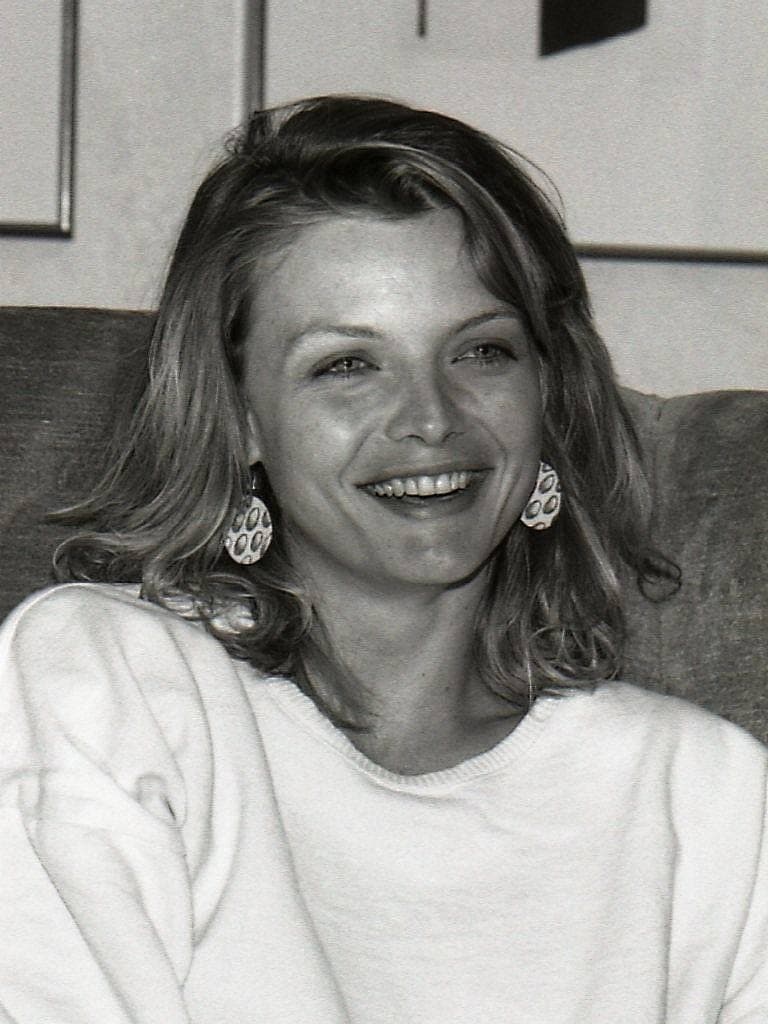 Michelle Pfeiffer smiling, in a white sweatshirt and drop earrings, in black and white