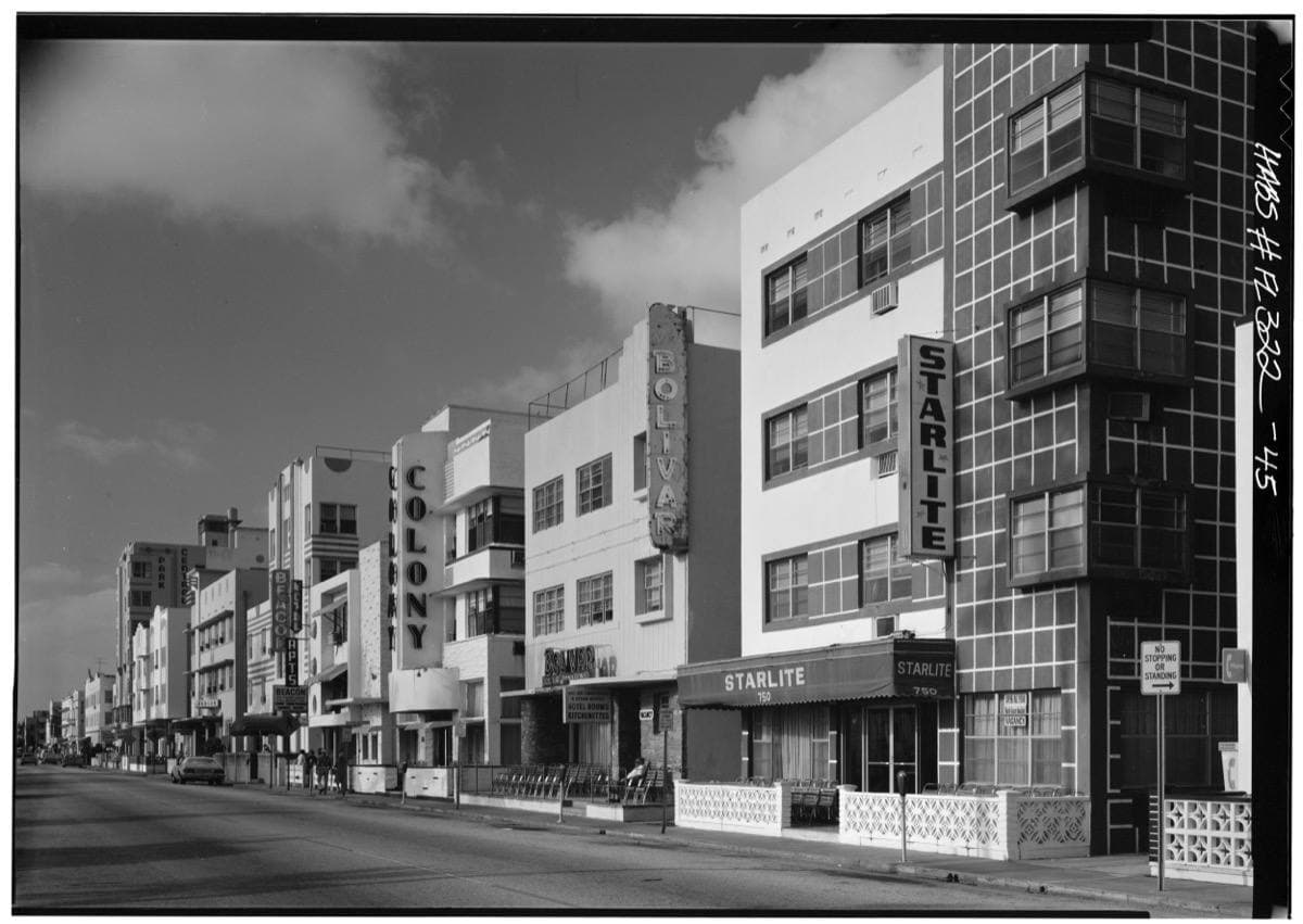 A black-and-white row of low Art Deco hotels with fins and signs along an empty street