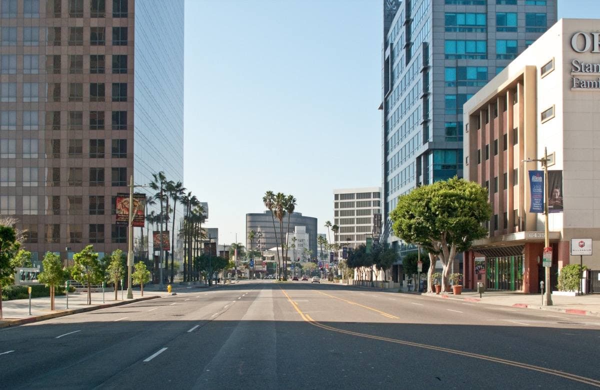A wide empty boulevard between office towers and palms, running towards Beverly Hills