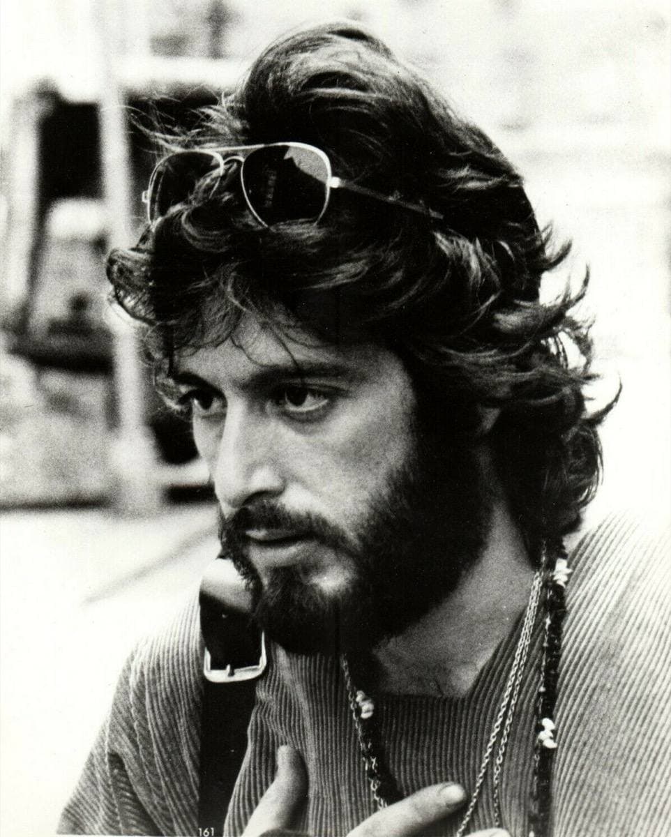 Al Pacino, bearded, with sunglasses pushed up into his hair, holding a telephone receiver