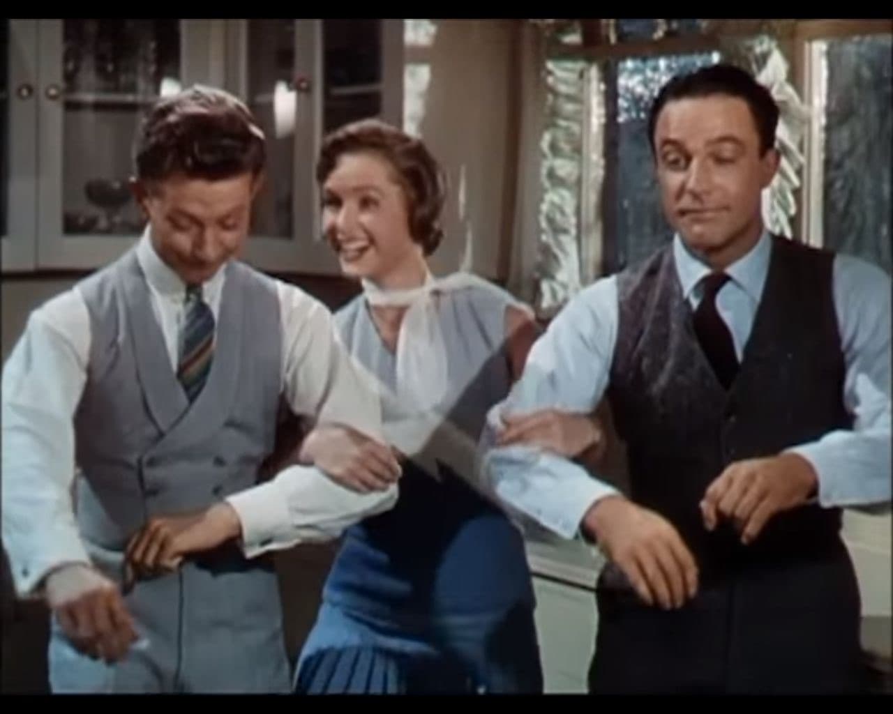 Donald O’Connor, Debbie Reynolds and Gene Kelly in a kitchen, arms linked, mid-dance
