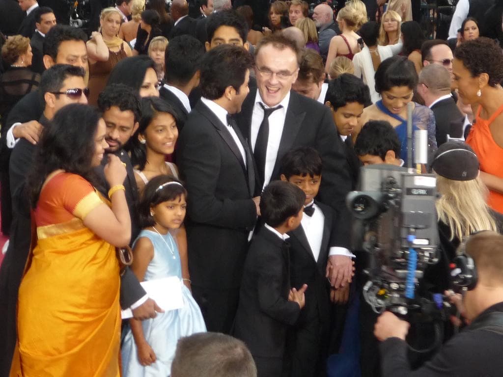 Colour photograph of a laughing man in a dinner suit surrounded by adults and children in evening wear on a crowded red carpet