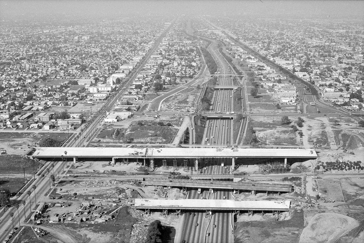 A black-and-white aerial view of freeway bridges under construction crossing a busy freeway
