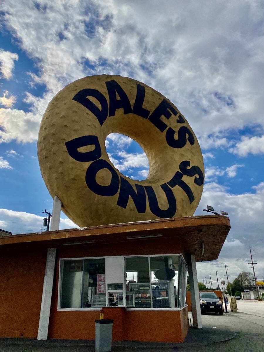 A small brick doughnut stand topped by a giant ring-shaped doughnut sign under a cloudy blue sky