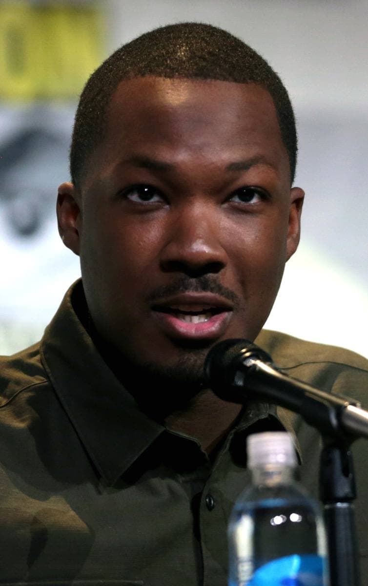 Corey Hawkins speaking into a microphone in an olive shirt