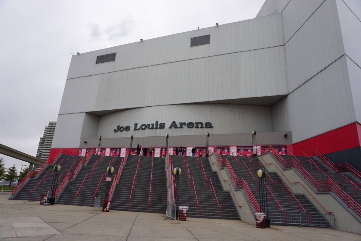 The pale grey front of a large arena with a wide red staircase