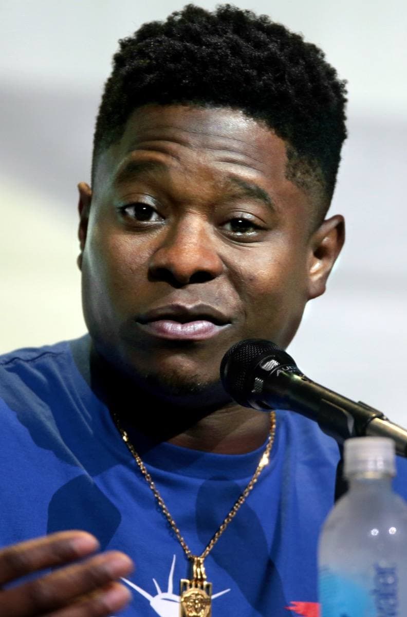Jason Mitchell speaking into a microphone in a blue T-shirt and a gold chain
