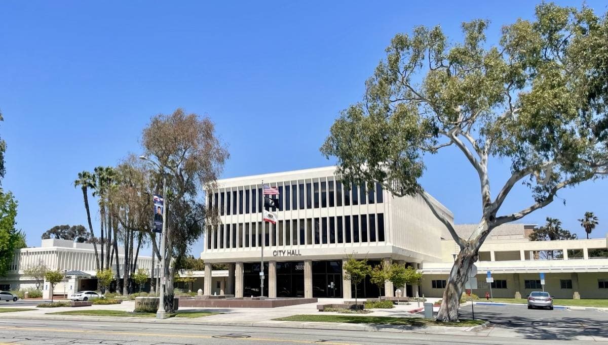 A low modern civic building behind lawns and palm trees