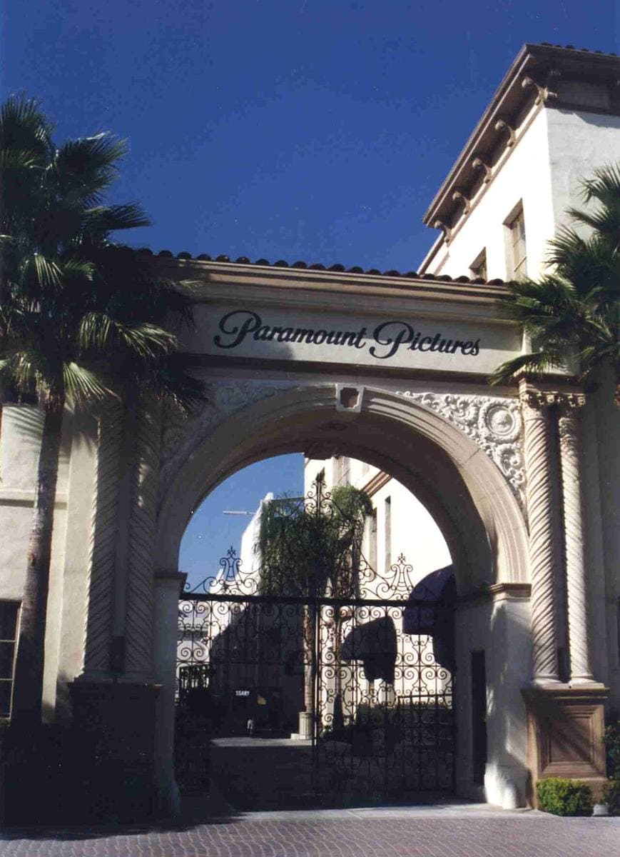 An ornate cream archway lettered Paramount Pictures, wrought-iron gates beneath, palms behind