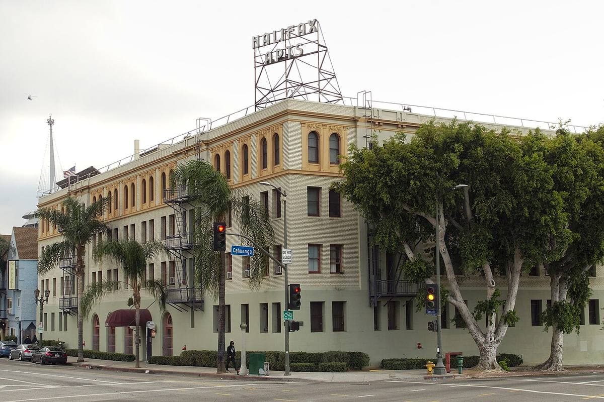 A cream 1920s apartment block on a street corner with palms and a rooftop sign