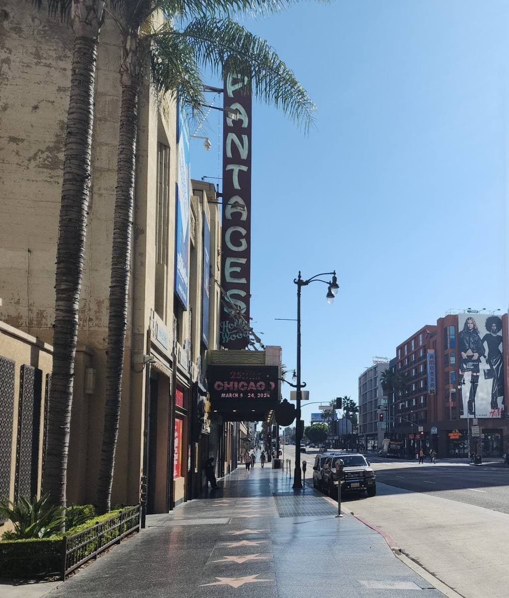 The tall vertical Pantages sign over a palm-lined Hollywood Boulevard pavement