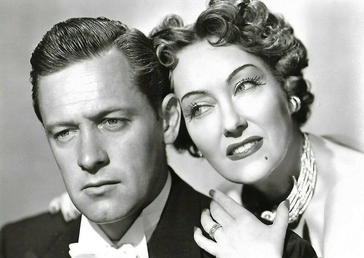 William Holden in a dinner jacket, Gloria Swanson leaning on his shoulder with a jewelled hand at his collar