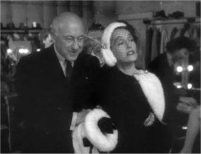 Cecil B. DeMille, smiling, with Gloria Swanson in a white fur hat and stole