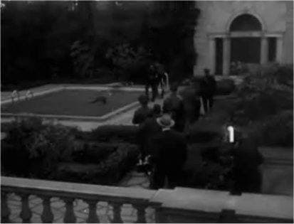 Police and photographers crowd the edge of a pool below a balustraded terrace and an arched house front