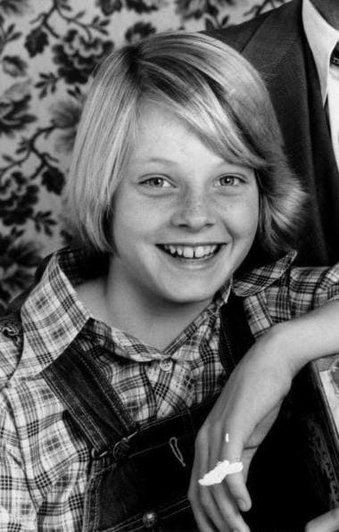 A smiling girl with a fair, straight fringe in a checked shirt and dungarees