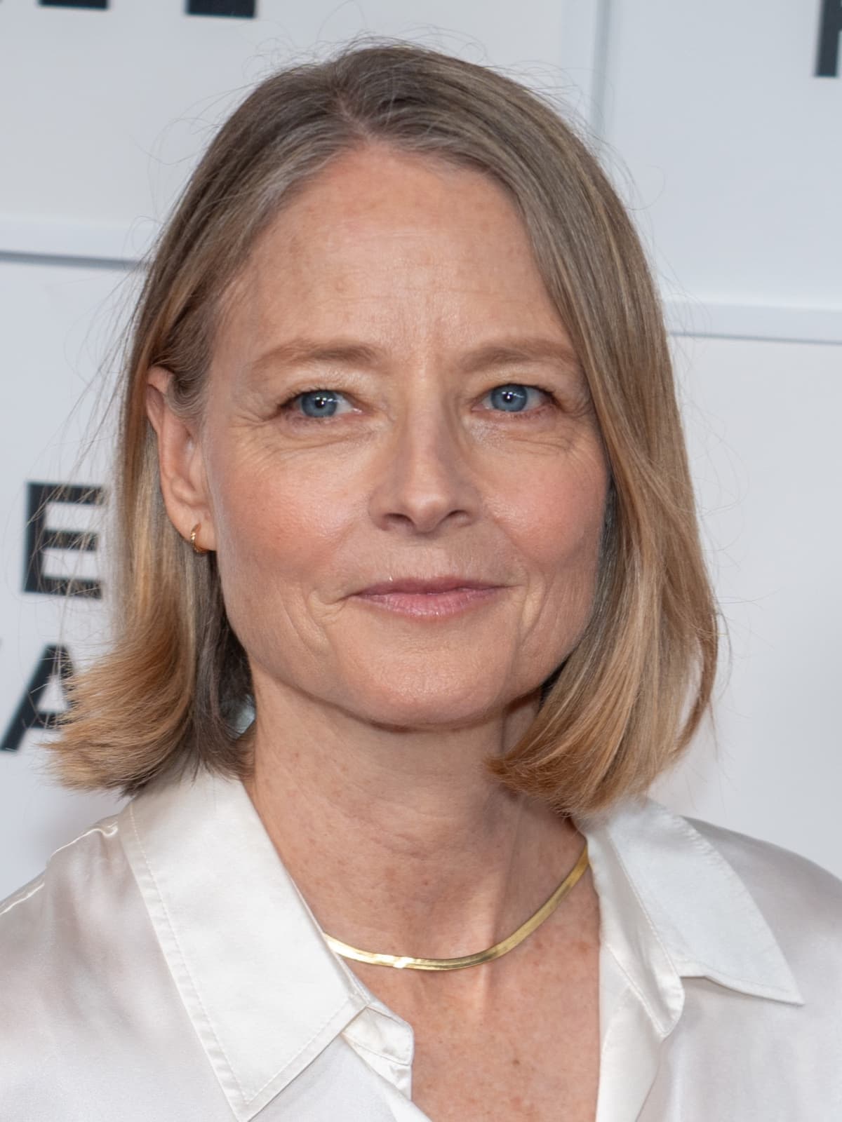 Jodie Foster, with a fair bob, smiling in a white silk shirt