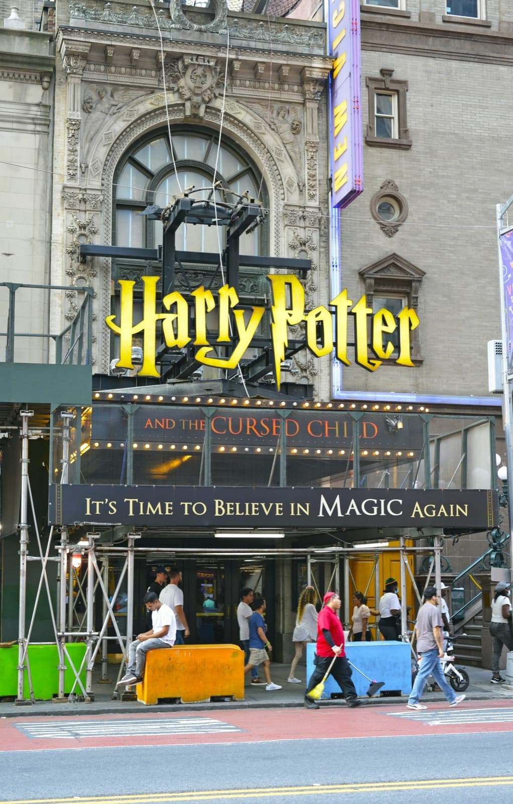 A gilded theatre arch with a large lit sign over the entrance, people on the pavement