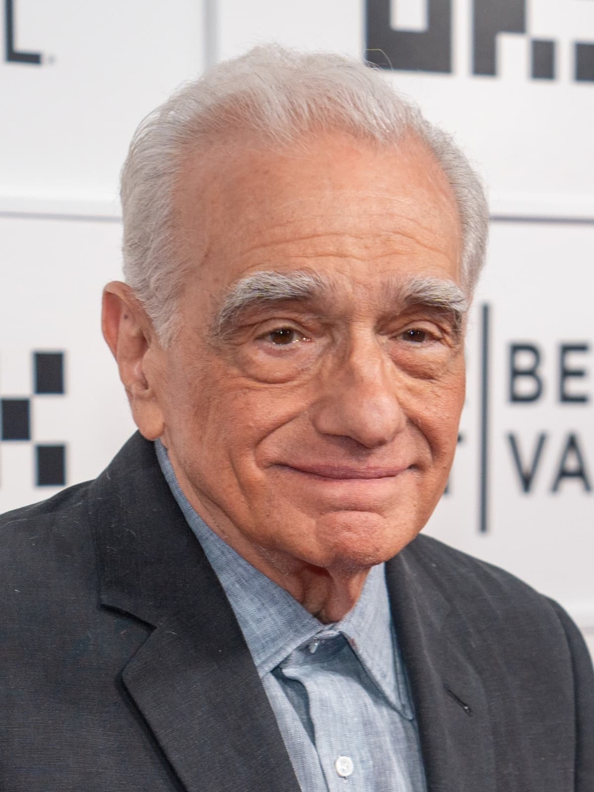 Martin Scorsese, white-haired and smiling, in a dark jacket and blue shirt
