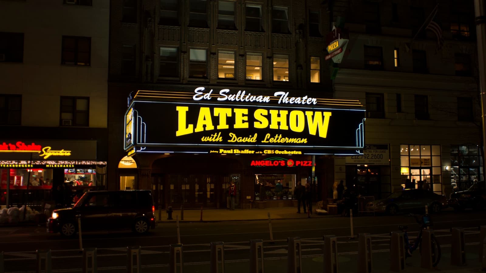 A theatre marquee lit yellow and blue at night on Broadway