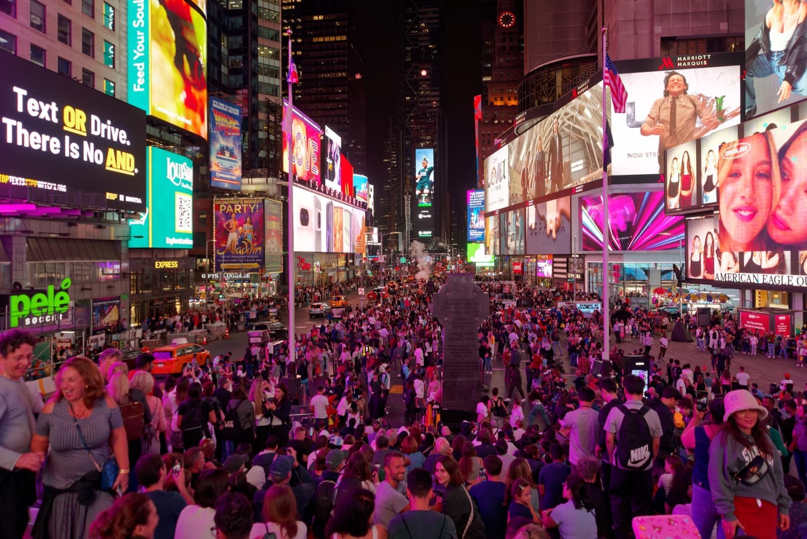 Times Square at night, crowds on the plaza under walls of bright screens