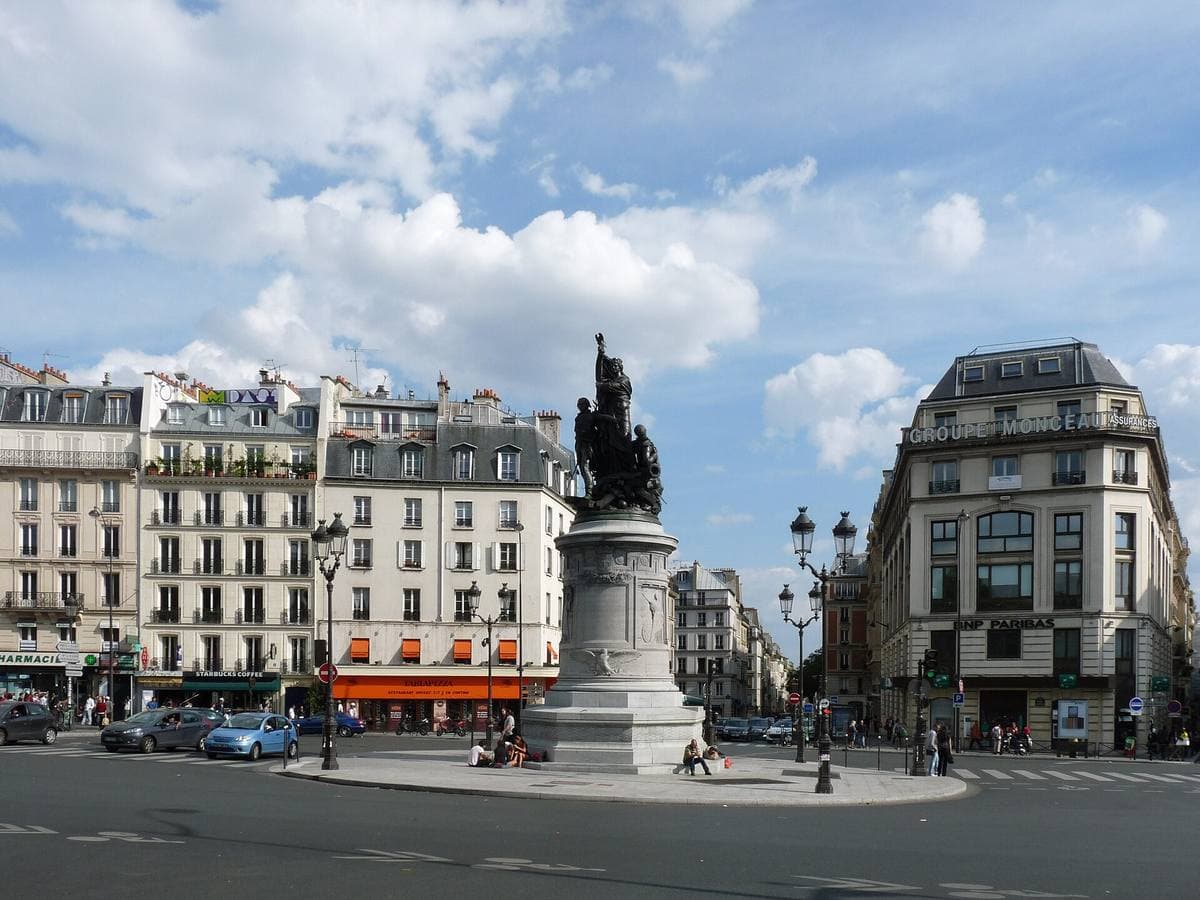 A wide square with a tall monument and old buildings around it