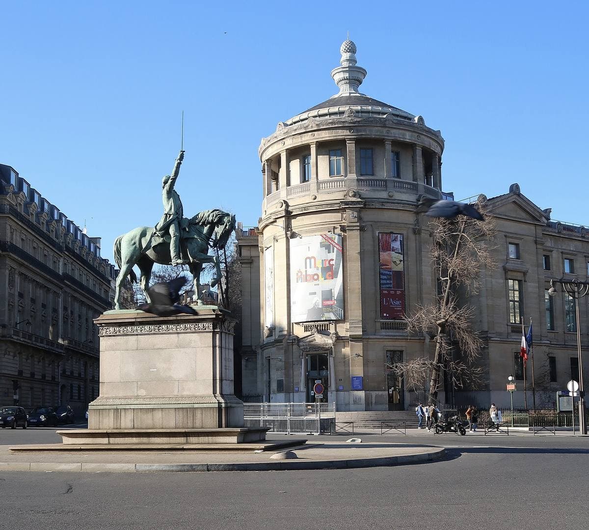 An equestrian statue on a stone plinth in front of a domed museum