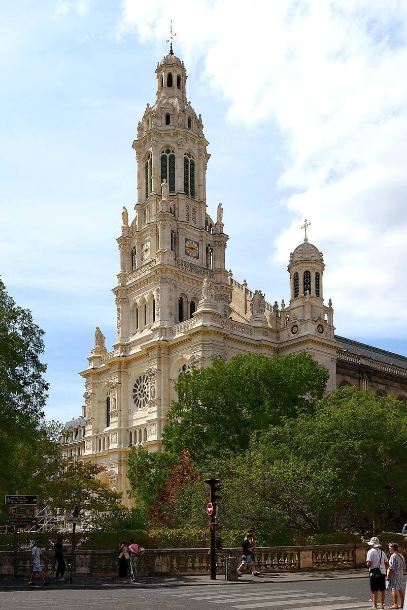 A tall stone church tower above trees and a square