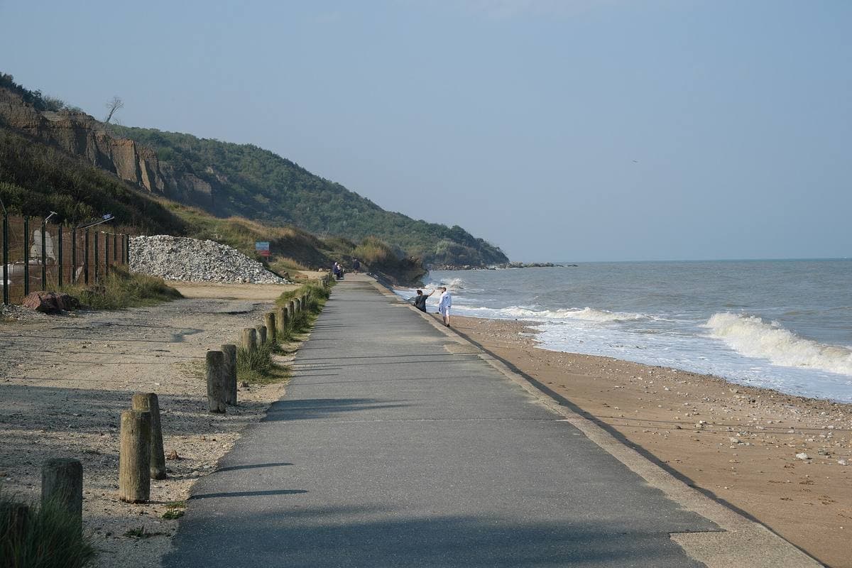 A seafront path running toward green cliffs