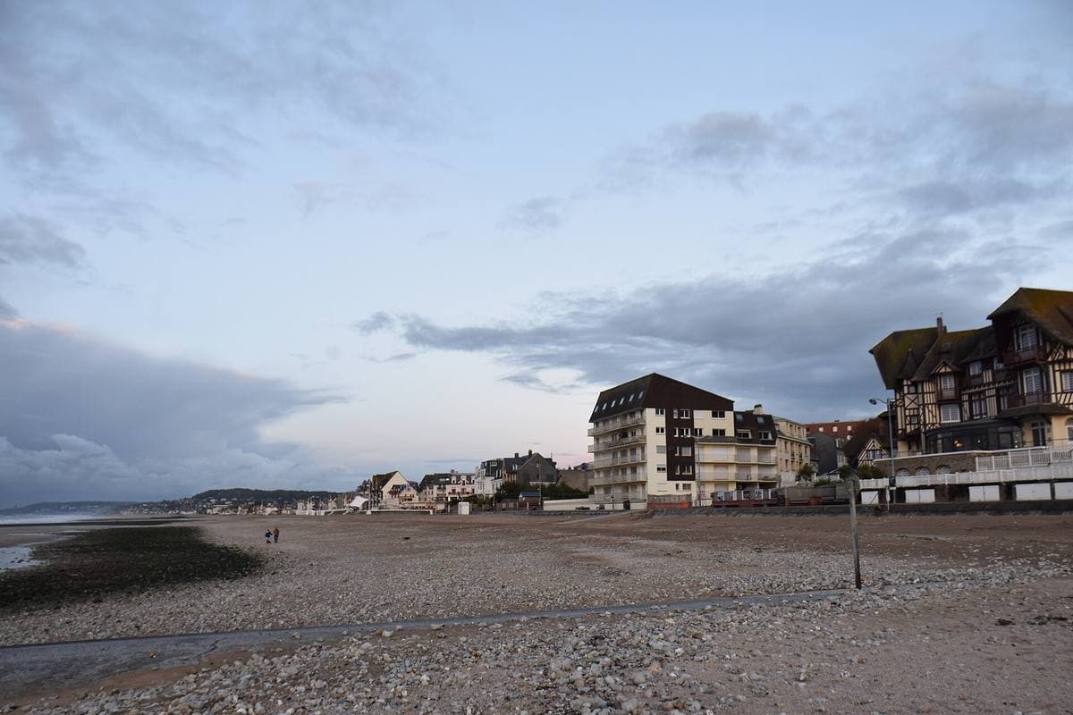 A wide grey beach at low tide with seaside villas behind
