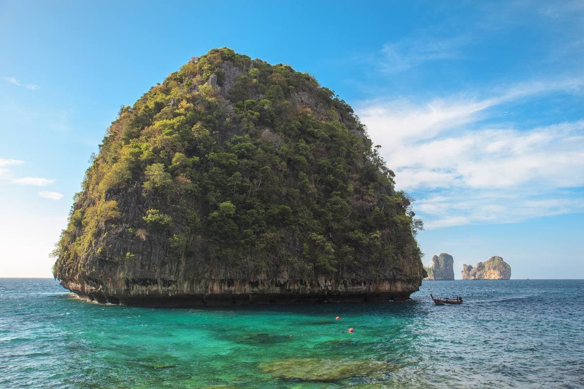 A rock standing in blue water at the mouth of a cove, cliffs behind