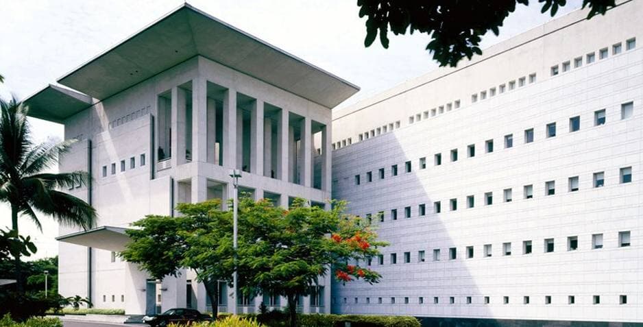 A low modern embassy building behind a fence and lawn
