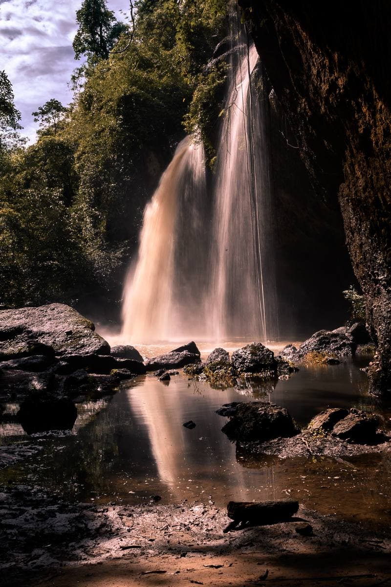 A broad waterfall pouring over a rock lip into a pool, framed by forest