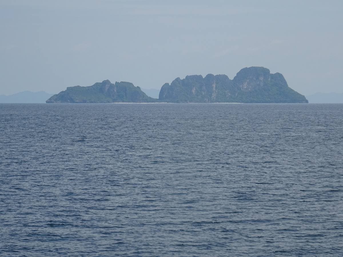 A steep forested island rising from a calm blue sea