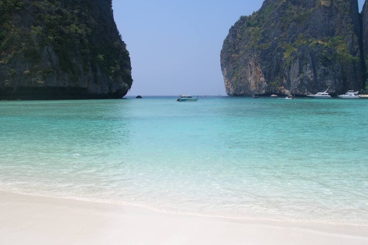 Turquoise shallows over white sand, with sheer limestone headlands either side and a few boats far out
