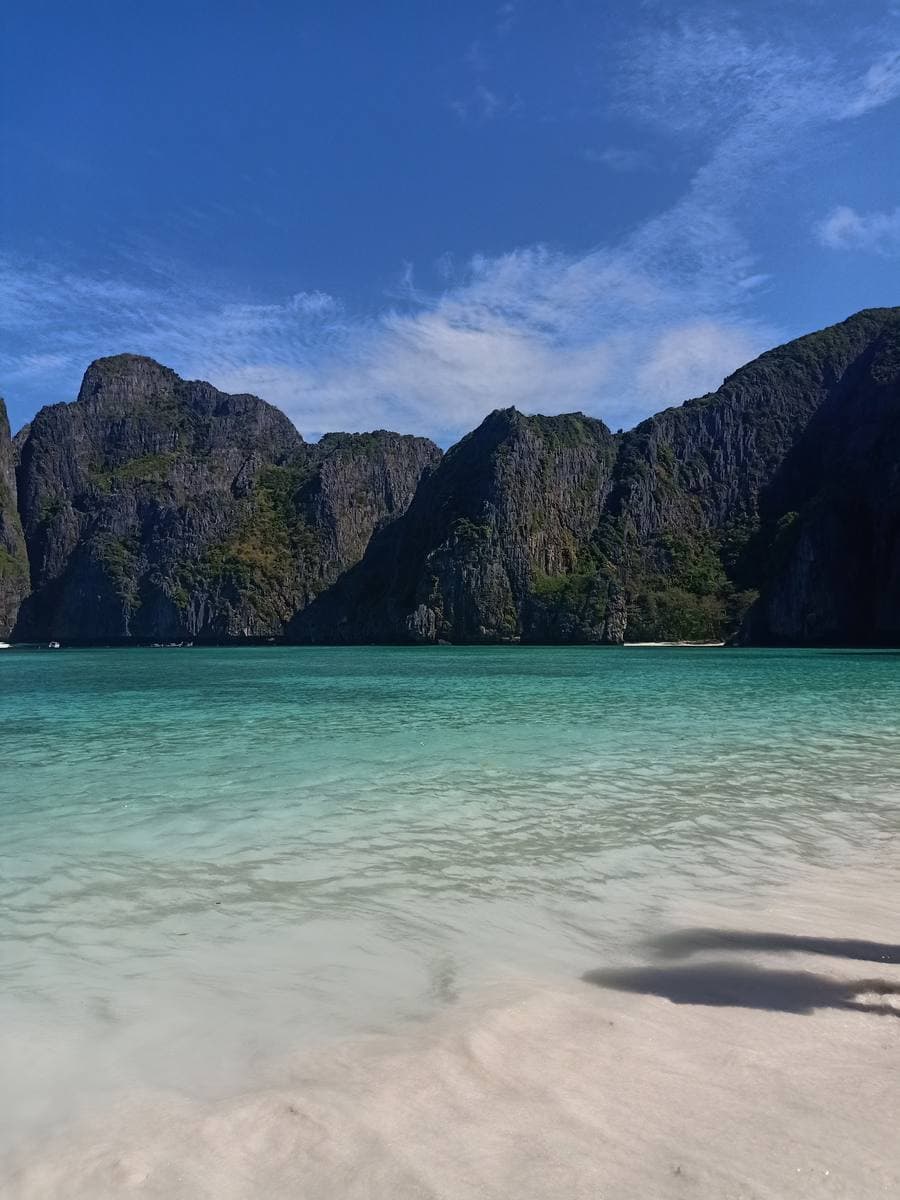 Clear green water over white sand, an empty shoreline and a limestone cliff behind